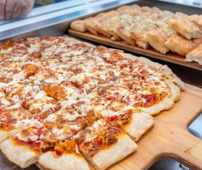 Quadratisch geschnittene Pizza auf einem Holzbrett.