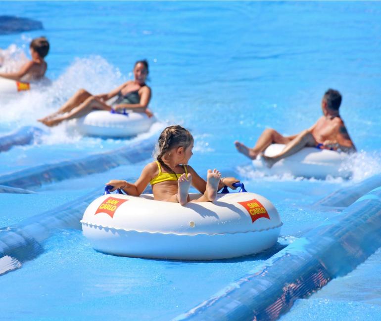 Persone felici su ciambelle galleggianti in un parco acquatico sotto il sole.