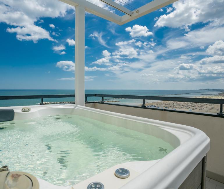 Vasca idromassaggio con vista mare, cielo azzurro e spiaggia lontana.