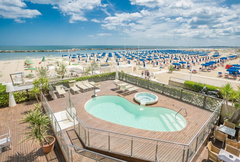 Piscina e spiaggia con ombrelloni colorati in una giornata soleggiata.