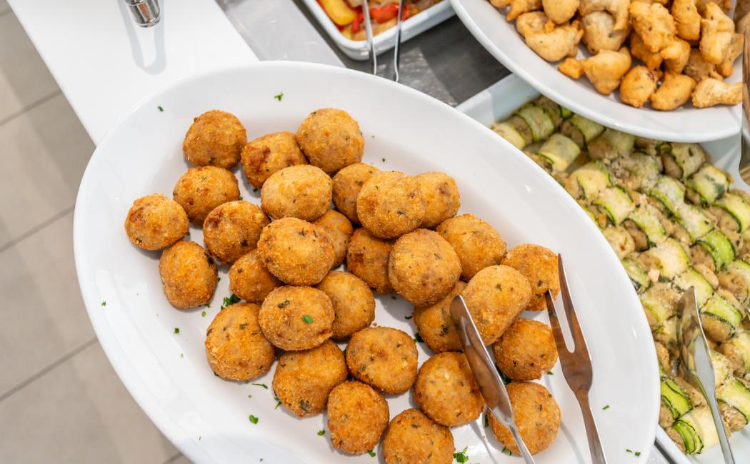 Polpette fritte su piatto bianco, servite con pinze per buffet.