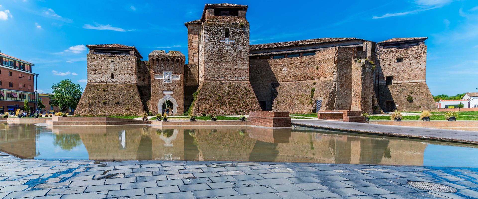 Antica fortezza in mattoni con fossato riflettente, sotto un cielo limpido e soleggiato.