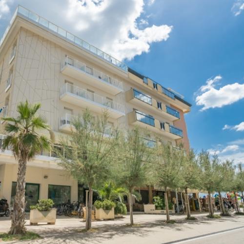 Edificio moderno con balconi, alberi e cielo blu con nuvole.