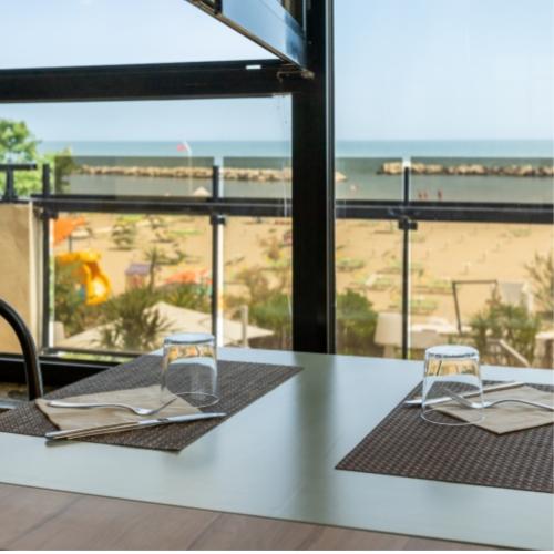 Tavolo apparecchiato con vista mare, spiaggia e ombrelloni in lontananza.