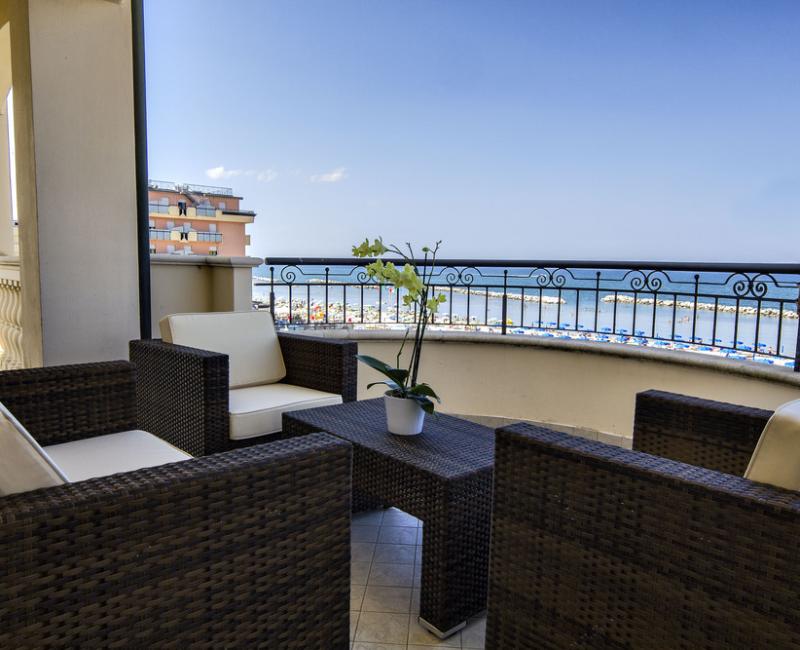 Terrazza con mobili in rattan, vista mare e spiaggia in lontananza.